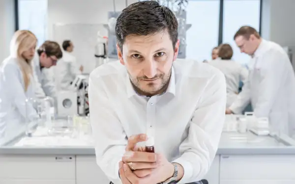 Mężczyzna w białej koszuli trzyma fiolkę z płynem, w tle laboratorium, gdzie pracują inni naukowcy. To kluczowe xtpl akcje.