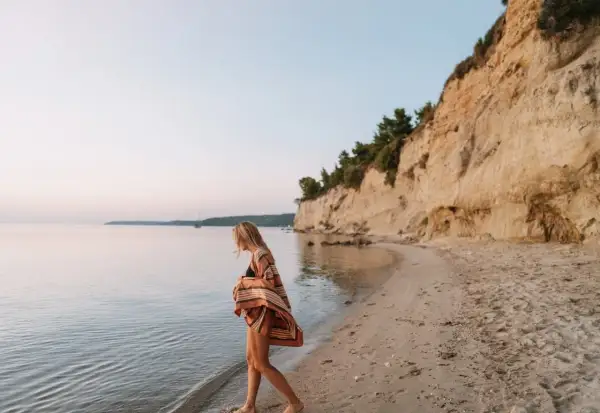 Mujer rubia camina por la playa, sintiendo la brisa marina. Ella anhela la libertad y el deseo de querer viajar sola.
