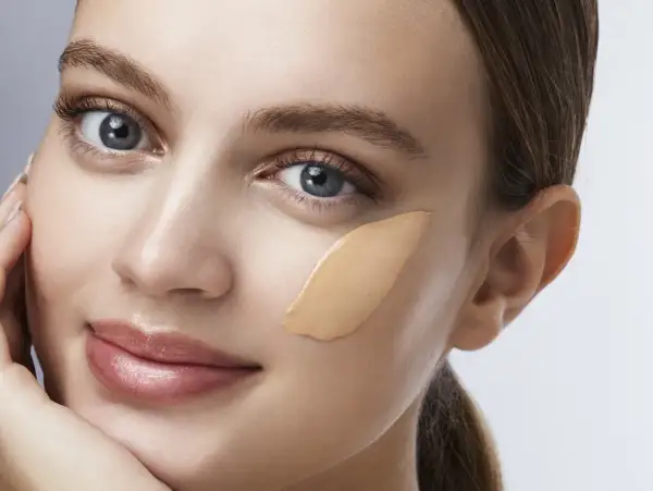 Una donna con un tocco di fondotinta sulla guancia, un esempio visivo di come applicare il fondotinta per un look naturale.