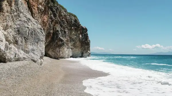 Skaliste klify otaczają kamienistą plażę Gjipe Beach, gdzie turkusowe morze łagodnie faluje.