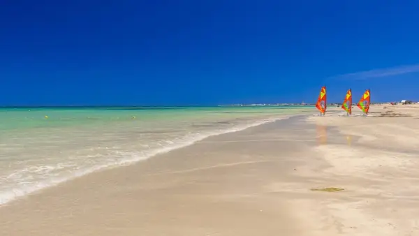 Piękna plaża w Tunezji w czerwcu. Idealna pogoda na windsurfing, trzy kolorowe żagle czekają na wiatr.
