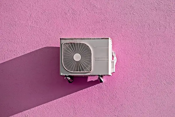 Unità esterna di condizionatore appesa a un muro rosa acceso, con ombra proiettata. Pensando allo smaltimento condizionatori.