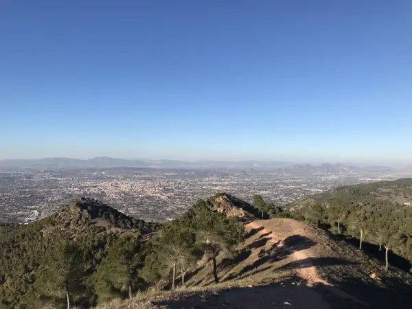 Vista panorámica desde la sierra de carrascoy, con un extenso paisaje urbano y montañas al fondo bajo un cielo azul despejado.