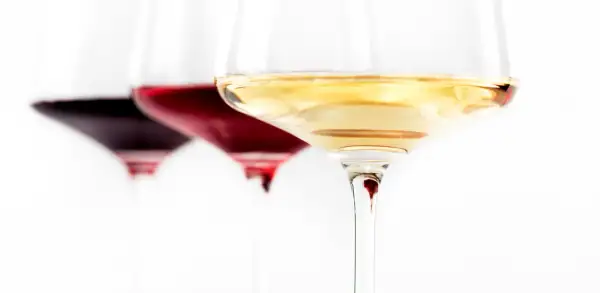 Trzy kieliszki z winem: ciemnoczerwonym, rubinowym i białym. Wino się pieni, tworząc subtelne refleksy.