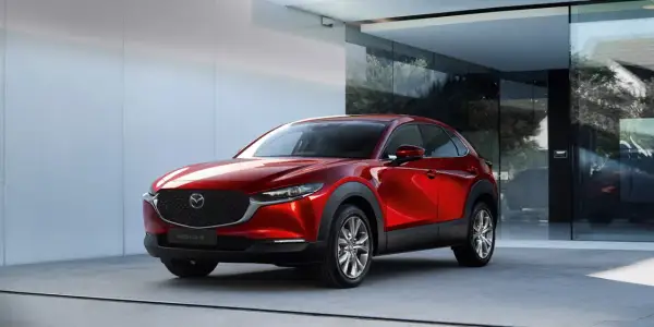 Elegancka, czerwona Mazda CX-30 błyszczy przed nowoczesnym budynkiem z dużymi oknami.