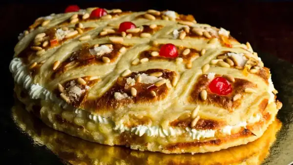 Deliciosa coca de San Juan rellena de crema, decorada con piñones, cerezas rojas y azúcar.