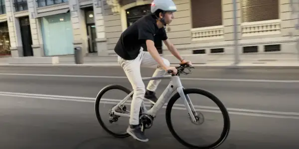Un joven con casco y ropa casual pedalea una bicicleta eléctrica por la ciudad.