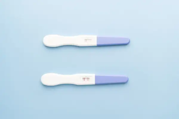 Dwa testy ciążowe na jasnoniebieskim tle. Jeden pokazuje jeden pasek, drugi dwa. Kiedy zrobić test ciążowy?