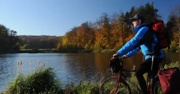 Jesień sprzyja jednodniowym wycieczkom rowerowym. Rowerzysta z plecakiem podziwia jesienne barwy lasu nad jeziorem.