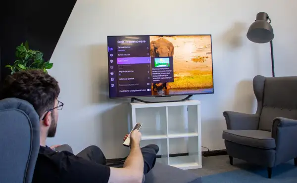 Mężczyzna siedzi w fotelu i ogląda telewizor z menu ustawień obrazu.