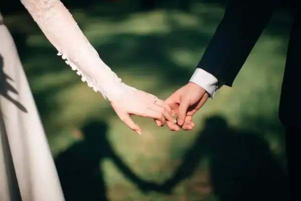 Dłoń panny młodej w koronkowej sukni i pana młodego w garniturze trzymają się za ręce. Zastanawiasz się, ile dać na wesele jednodniowe?