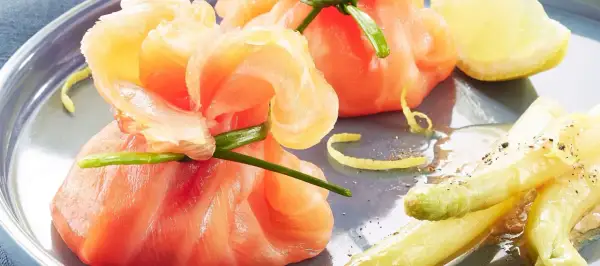 Une délicieuse entrée froide : des fagots d'asperges et de saumon fumé, ornés d'une touche de citron et de ciboule.