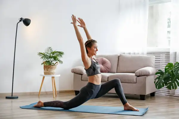 Une femme souriante pratique le yoga à la maison, profitant des bienfaits de cette discipline pour son bien-être.