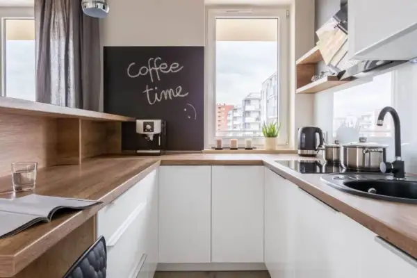 Biała kuchnia z drewnianym blatem, na którym stoi ekspres do kawy. Na tablicy napis "coffee time".