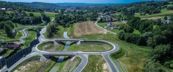 Nowoczesny węzeł drogowy na drodze krajowej 75, z mostami nad rzeką, otoczony zielonymi wzgórzami i domami.