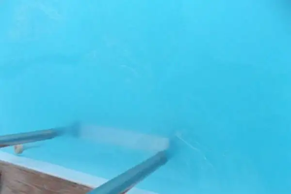 Un rouleau nettoie l'eau trouble d'un bassin bleu vif, laissant des traces blanches.