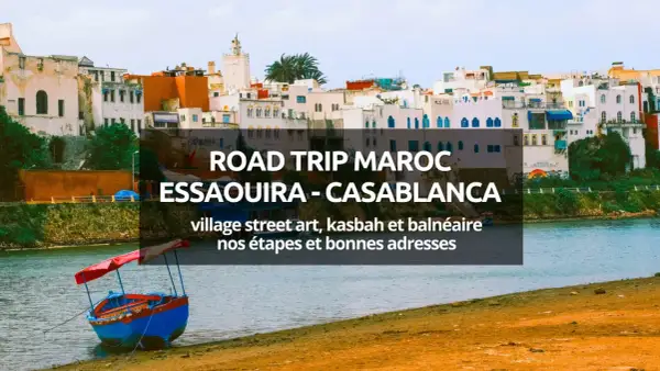 Bateau coloré sur la rive d'une ville côtière marocaine, avec des bâtiments blancs et bleus en arrière-plan.