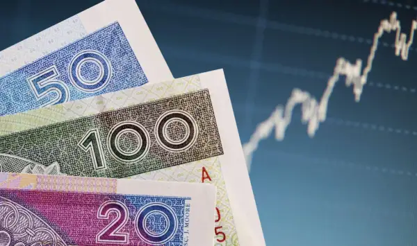 Polskie banknoty 20, 50 i 100 zł na tle wykresu giełdowego. Czy pieniądze w banku są bezpieczne?