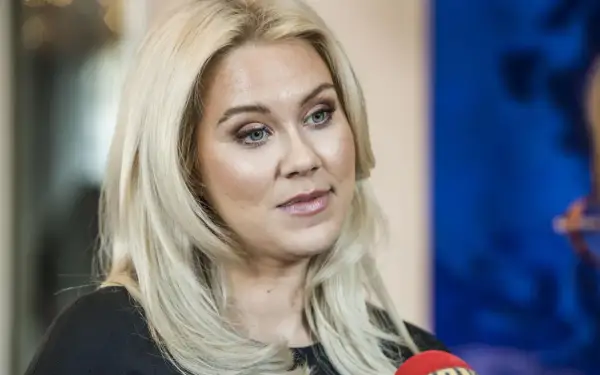 Caroline Hainer, med blont hår och makeup, ser åt sidan. En mikrofon syns i förgrunden.