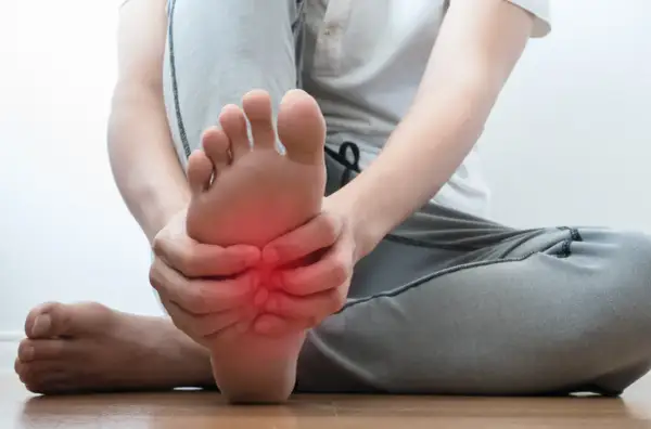 Persona che si tiene il piede, con un'area rossa che indica dolore sotto pianta del piede al centro.