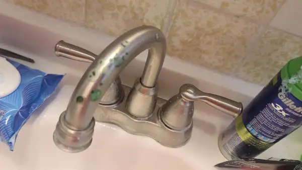 Rubinetti del bagno con calcare verde incrostato. Accanto, salviettine e una bomboletta di schiuma da barba.