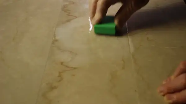 Mano che lucida un marmo corroso con una spugna verde.