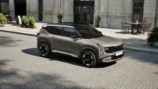 Nowy model Kia, szary SUV, parkuje na brukowanej ulicy przed eleganckim budynkiem.