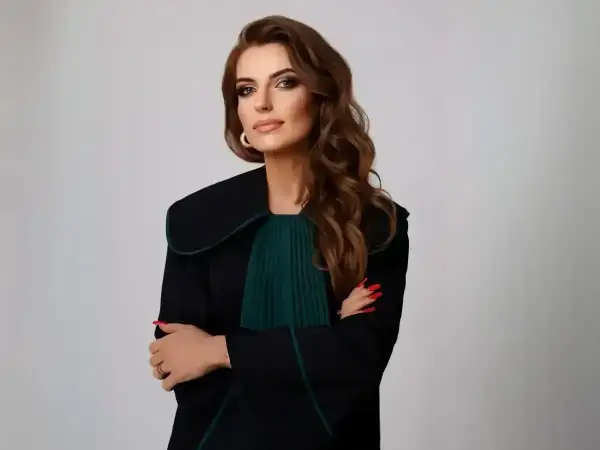 Kobieta w todze prawniczej, z rękami skrzyżowanymi na piersi, na jasnym tle.