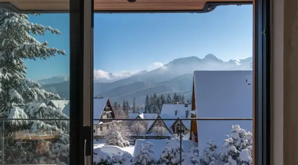 Zimowy krajobraz z ośnieżonymi domkami i lasem, idealny na nocleg z pięknym widokiem na Tatry.
