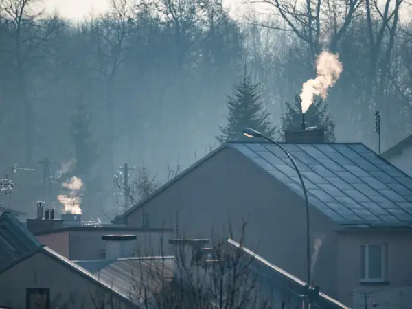 Dym z komina nad domami, czy spaliny z pieca gazowego są szkodliwe? Mglisty poranek nad miastem.