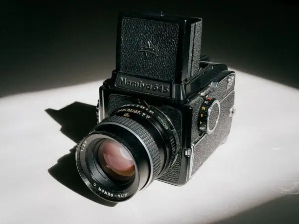 A classic Mamiya 645 medium format camera sits on a white surface, bathed in dramatic light and shadow.