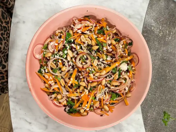 En färgstark ris sallad med jordnötter, morötter, rödlök och örter i en rosa skål.