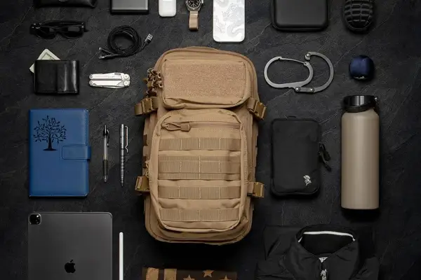 Un bolso molle de color caqui, listo para la aventura, rodeado de elementos esenciales: cartera, navaja, tablet, bolígrafos, botella de agua y más.