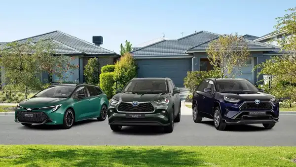 Trzy modele toyoty crossover: zielona Corolla Touring Sports, ciemnozielony Highlander Hybrid i granatowy RAV4 Plug-in Hybrid, stoją przed domami.