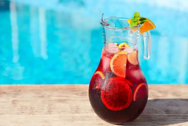 Pichet de sangria recette, rempli de fruits et de glaçons, prêt à être dégusté au bord de la piscine.