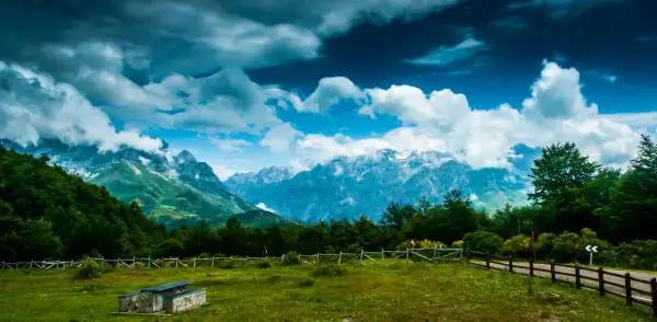 Majestuoso mirador de los Picos de Europa con nubes dramáticas sobre picos nevados y un prado verde.