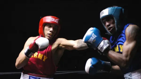 Two boxers, one in red with "ARMY" on his vest, the other in blue, engage in intense **sparring**. Their gloves are raised, ready for the next move in this practice bout.