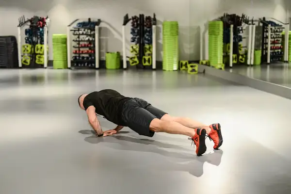 Mężczyzna wykonuje pompki diamentowe na siłowni, ćwicząc klatkę piersiową i triceps.