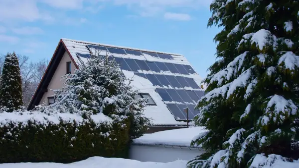 Schneebedeckte Solaranlage auf einem Hausdach, die zeigt, wie man im Winter heizen kann.