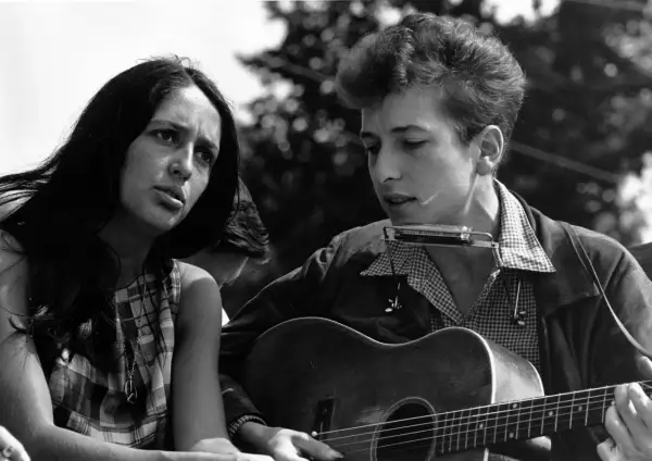 Młody Bob Dylan gra na gitarze i harmonijce, obok siedzi kobieta. To obraz z czasów, gdy jego twórczość zasłużyła na nagrodę Nobla.