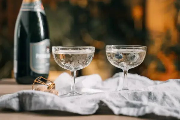 Dwa kieliszki z musującym winem, jeden z borówkami, obok butelka i korek. Czy wino musujące to szampan?
