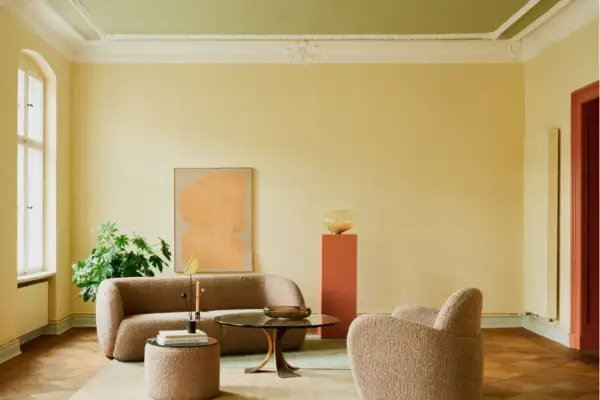 Sanfte gelbe Wände mit einer dezenten Streichtechnik Wand, kombiniert mit einem grünen Deckenanstrich, schaffen eine warme Atmosphäre. Ein beiger Bouclé-Sofa und Sessel laden zum Entspannen ein.