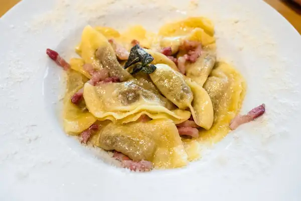 Casoncelli alla bergamasca, pasta ripiena con pancetta e salvia, spolverati di parmigiano su un piatto bianco.