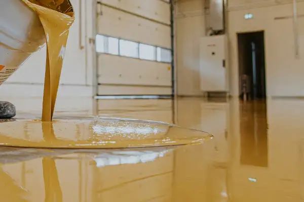 Liquido giallo, probabilmente resina epossidica cos'è, cola da un secchio su un pavimento lucido in un capannone.