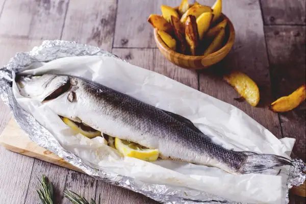 Gegrillter Seebarsch mit Zitrone, bereit für den köstlichen Geschmack. Dazu knusprige Kartoffelspalten.