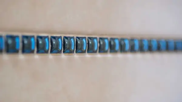 Ligne de petites mosaïques bleues, comme une frise, à une certaine hauteur sur un mur de salle de bain.