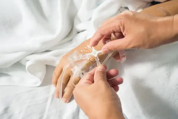 Ręce pielęgniarki podłączają kroplówkę do portu do podawania chemii na ręce pacjenta.