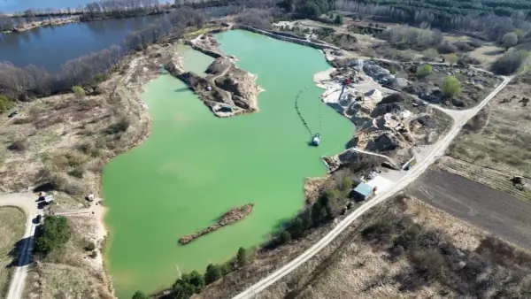 Widok z lotu ptaka na turkusowe jezioro zajączkowskie, otoczone piaskowymi skarpami i zielenią. Widać sprzęt wydobywczy i łódź.