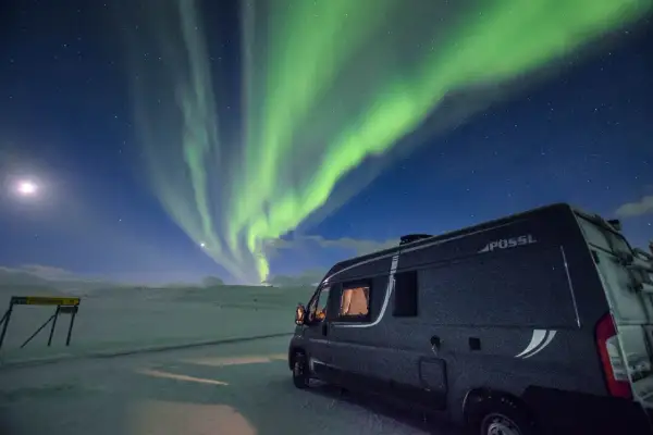 Ein Wohnmobil steht unter dem faszinierenden Himmel, wo grüne **polarlichter** tanzen. Mond und Sterne leuchten über der verschneiten Landschaft.