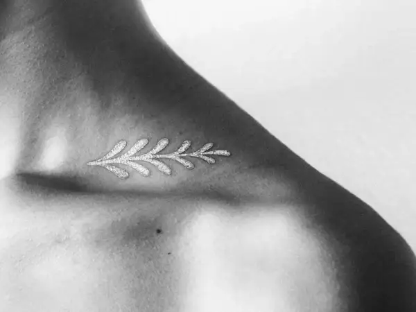 Delicado diseño de rama con **tatuajes blancos en piel negra**, resaltando la delicadeza y el contraste en el hombro.